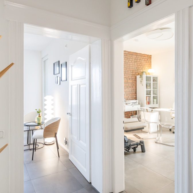 Praxisräume Heller Flur mit Blick auf einen Raum mit Therapieliege und Vitrinenschrank.