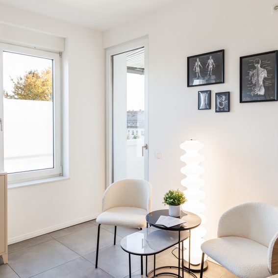 Wartebereich Heller Sitzecke mit zwei Stühlen, Tisch, Lampe und Bildern an der Wand.